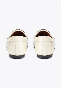 Roomkleurige leren loafers met een krokodillenstructuur en een lage zwarte zool, voorzien van een decoratief gouden sierstuk aan de voorkant.