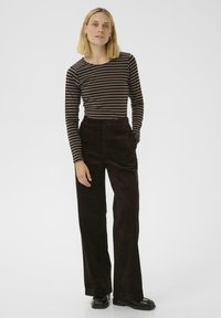 Pantalons en velours côtelé noir à jambes larges assortis à un haut à rayures brun et noir à manches longues. La tenue présente une coupe décontractée et un tissu texturé.