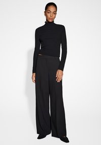 Un pull à col roulé noir côtelé associé à un pantalon large noir taille haute. Design minimaliste, texture lisse et silhouette ajustée.