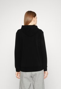 Svart hettegenser med en myk tekstur, som har snor i hetta og ribbestrikket nederkant. Baksiden viser en avslappet passform og minimalistisk design.