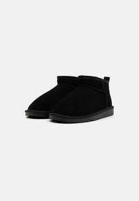 Botas de tobillo de ante negro con punta redonda, panel lateral elástico y suela de goma plana. Presentan un diseño simple y minimalista sin adornos.