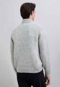 Suéter gris claro de punto con cuello alto y dobladillo acanalado, con una textura suave y un ajuste relajado, mostrado desde atrás.