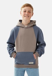 Huppari, jossa on kaksivärinen muotoilu harmaassa ja sinisessä, etutasku ja poimutetut hihansuut. Pehmeä, tekstuurinen kangas.