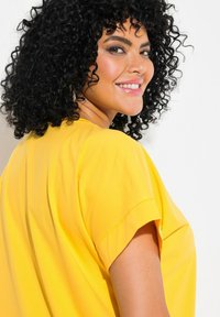 Top amarillo de manga corta con un corte holgado y una textura suave y lisa. Diseño sencillo con un escote redondo y puños enrollados.