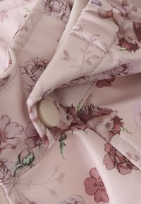 Blommönstrad tyg i mjuka rosa nyanser med knappstängning, slät textur och delikata sömnadsdetaljer.