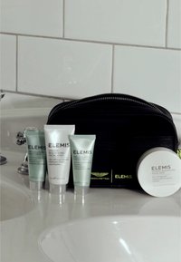 Borsetta nera con zip con il marchio "ELEMIS" in bianco e verde. Contiene tre tubetti argentati e verdi e un barattolo rotondo di prodotti per il viso.