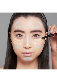Application de maquillage mettant en vedette diverses crèmes colorées sur le visage. Les teintes comprennent du jaune pâle, du vert et de la lavande, disposées en lignes et en points.