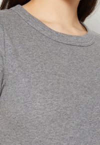 Grå ribbad tröja med klassisk rundad halsringning och mjuk textur, som framhäver subtila variationer i tygens tjocklek.