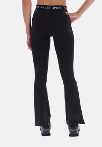 Čierne športové nohavice so širokými nohavicami a vysokým pásom, na ktorých je logo "TED BAKER SPORT". Materiál sa zdá byť elastický a hladký, ideálny na pohyb.