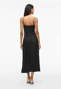 Vestido midi de satén negro con tirantes finos y una silueta fluida, que presenta una textura suave y un diseño minimalista. Se muestra la vista posterior.