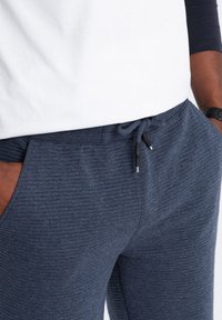 Pantaloni jogger blu navy con un tessuto texturizzato, vita con cordoncino e tasche laterali. Il dettaglio delle cuciture visibili aggiunge un design sottile.