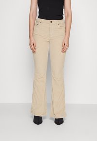 Beige manchesterbyxor med vid fåll, framfickor, bältesöglor och knappstängning, kombinerade med svarta ankelboots med klack.