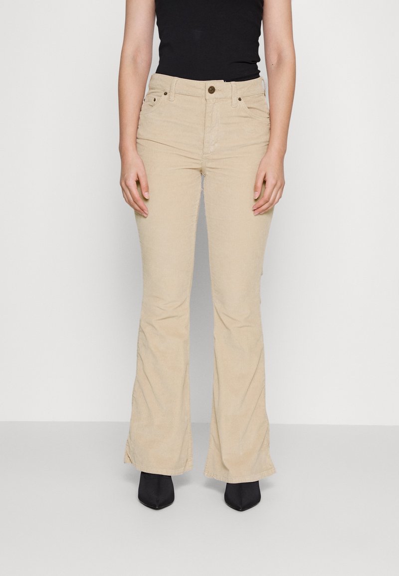 Beige manchesterbyxor med vid fåll, framfickor, bältesöglor och knappstängning, kombinerade med svarta ankelboots med klack.