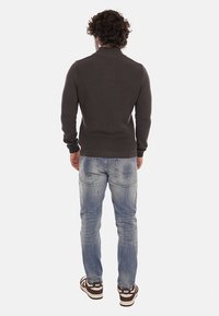 Maglione lavorato a maglia grigio scuro con colletto alto, abbinato a jeans chiari strappati e sneakers marroni con dettagli bianchi.