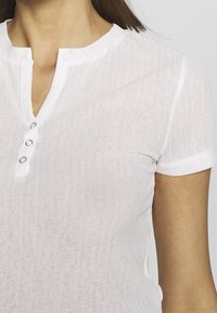 White short-sleeved shirt with a henley design. Features a round neckline, three-button placket, and a textured fabric.