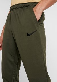 Gröna sweatpants med en svart Nike-logotyp, utrustade med resårmidja och sidofickor, tillverkade av ett mjukt, texturerat tyg.