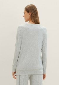 Maglietta grigia chiara a maniche lunghe con scollatura rotonda, maniche raglan e vestibilità rilassata. Tessuto morbido con una consistenza liscia. Nessun motivo visibile.