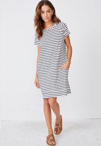 Sukienka w paski na krótki rękaw w kolorze granatowym i białym, o luźnym kroju, z okrągłym dekoltem i bocznymi kieszeniami, zestawiona z brązowymi sandałami.