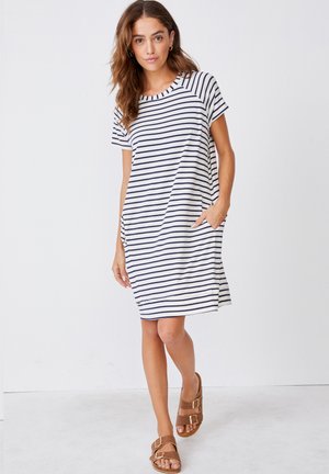 Sukienka w paski na krótki rękaw w kolorze granatowym i białym, o luźnym kroju, z okrągłym dekoltem i bocznymi kieszeniami, zestawiona z brązowymi sandałami.