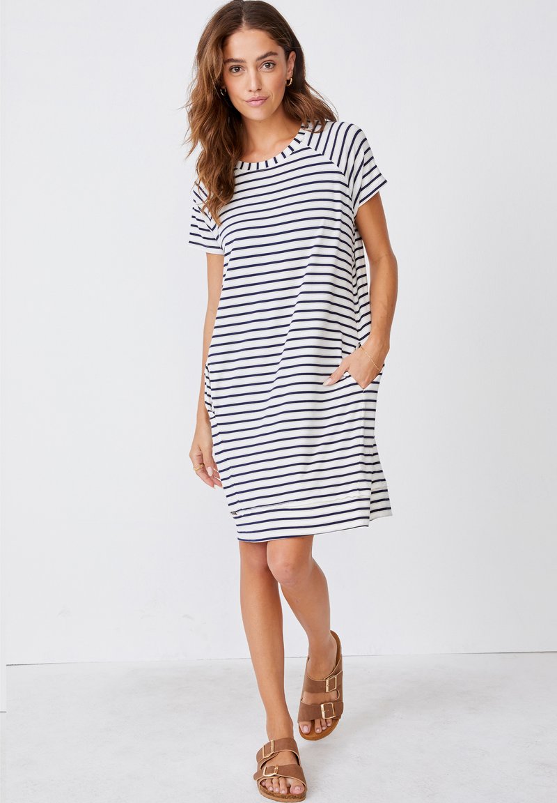 Sukienka w paski na krótki rękaw w kolorze granatowym i białym, o luźnym kroju, z okrągłym dekoltem i bocznymi kieszeniami, zestawiona z brązowymi sandałami.