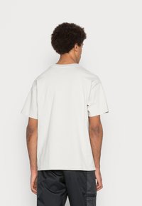 T-paita lyhyillä hihoilla, pyöreällä kaula-aukolla, vaaleassa beigen värissä. Valmistettu puuvillasta, siinä on rento muotoilu, sileä rakenne ja ei näkyviä kuvioita.