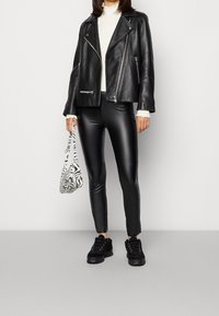 Schwarze Lederbikerjacke, gerippter weißer Pullover, schwarze glänzende Leggings und klobige schwarze Sneakers. Zebra-Muster Handtasche mit kurzen Tragriemen.