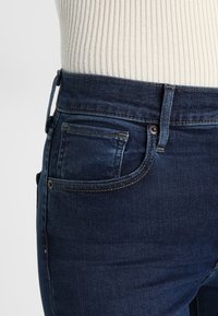 Dunkelblaue Denim-Jeans mit einer figurnahen Passform, die im klassischen Fünf-Taschen-Stil gehalten sind und sichtbare Nähte entlang der Nähte aufweisen.