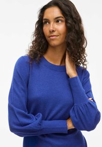 Maglione blu reale con scollatura tonda, polsini a coste e maniche a palloncino. Realizzato in un morbido tessuto a maglia, presenta una superficie liscia e fine.