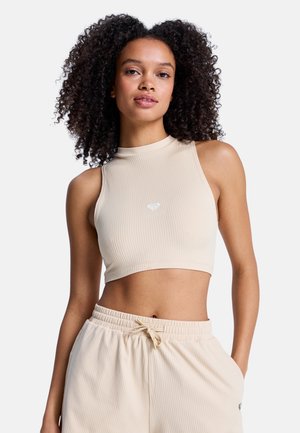 Beiges, geripptes Crop-Top mit hohem Kragen und kleinem Logo auf der Brust, kombiniert mit passenden beigen Hose mit Tunnelzug.
