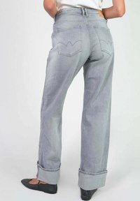 Jeans en denim gris taille haute avec une coupe ample. Présentent des ourlets roulés et une couture distinctive des poches arrière ressemblant à un motif de vague.