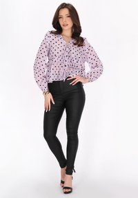 Lavendelbluse med polka dots og flæsekrave og ærmer, parret med højhvide sorte leggings. Sorte hæle fuldender outfittet.