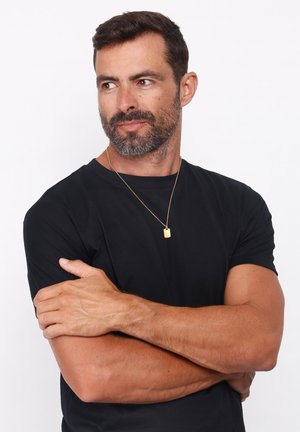 Schwarzes kurzärmeliges T-Shirt, getragen von einem Mann, mit einer goldenen Anhänger-Halskette. Der Hintergrund ist klar weiß, was die Kleidung und Accessoires hervorhebt.