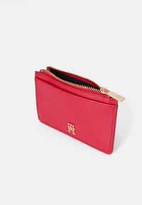 Piros bőr pénztárca arany cipzárral, középen egy kis logóval. Sima felület, téglalap alak, és cipzáras záródás.