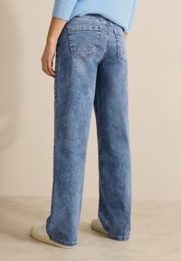 Jeans de mezclilla azul claro con ajuste recto, que cuentan con bolsillos traseros y sutiles acentos decorativos cerca de los dobladillos.