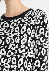 Pull en tricot à imprimé léopard noir et blanc avec un col rond, porté par une personne à la peau claire.