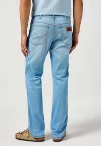 Pantalones vaqueros de mezclilla azul claro con un corte recto, bolsillos traseros con un diseño de zigzag y una etiqueta de cuero marrón en la cinturilla.
