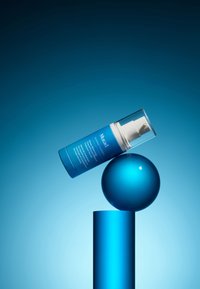 Klarer blauer Kunststoff-Pumpspender mit der Aufschrift "Murad Blemish Control", der auf einer glänzenden blauen Kugel lehnt, die auf einer zylindrischen blauen Säule balanciert.