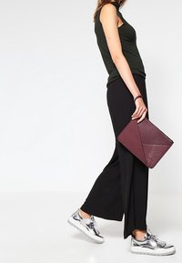 Pantalones anchos negros combinados con una blusa sin mangas verde oscuro, zapatillas plateadas y un bolso texto burdeos.