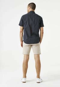 Chemise bleu marine à manches courtes avec un motif géométrique, associée à un short beige et des baskets blanches avec des accents bleus.