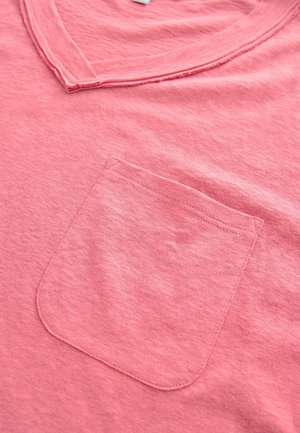 Rosa Baumwoll-T-Shirt mit V-Ausschnitt und einer einzelnen Brusttasche mit sichtbaren Nähten. Der Stoff hat eine weiche, strukturierte Oberfläche.
