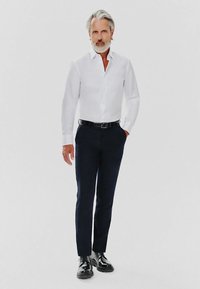 Biała koszula z długim rękawem, w połączeniu z ciemnoniebieskimi spodniami slim-fit i wypolerowanymi czarnymi butami. Gładkie tekstury i klasyczny design.