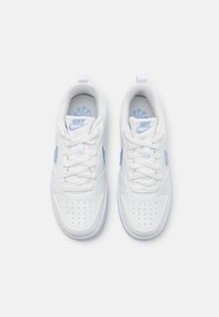 Pár bílých tenisek Nike s světle modrými logy swoosh, tkaničky svázané a perforovaná špička, pohled zhora na bílém pozadí.