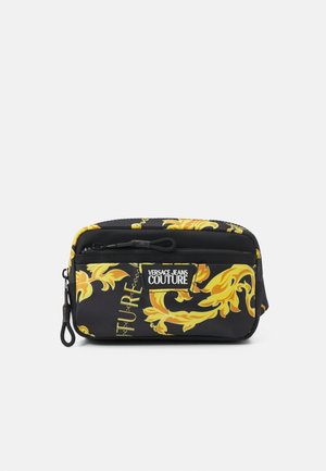 Pochette rectangulaire noire avec motif floral baroque jaune, poche avant zippée et étiquette "Versace Jeans Couture".