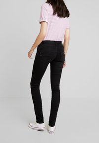 Czarne wąskie dżinsy o gładkiej strukturze, z tylnymi kieszeniami zapinanymi na guziki, w połączeniu z różową koszulą w paski i białymi trampkami.