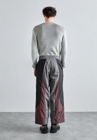 Pull en maille gris ; pantalon gris et noir avec des accents bordeaux ; coupe ample ; taille élastique ; texture lisse ; longueur cheville.
