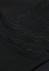 Zwart textiel met een gestructureerd oppervlak, gekenmerkt door gelaagde golfpatronen en naaddetails. Het materiaal lijkt lichtgewicht en enigszins doorschijnend.