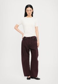 T-shirt a maniche corte crema abbinato a jeans larghi bordeaux scuri e ballerine nere, esposto su uno sfondo neutro.