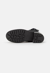 Botín negro hasta el tobillo con suela de goma. Patrón de tracción texturizado en la suela. Cuenta con cordones y parte superior de ante con diseño de punta curva.