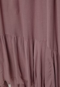 Tissu léger de couleur rouille avec une texture douce ; présente des couches plissées et des finitions effilochées pour un look décontracté.