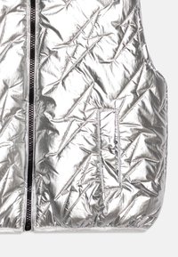 Gilet a soffietto argento con finitura lucida, motivo trapuntato a forme triangolari e chiusura frontale con zip rifinita in nero.
